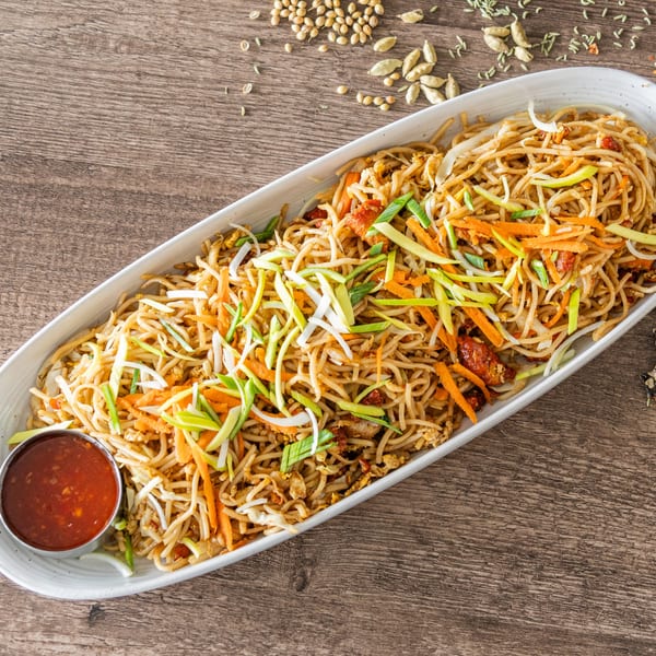 Indian Hakka noodles with vegetables and chicken, served with a side of chili sauce.