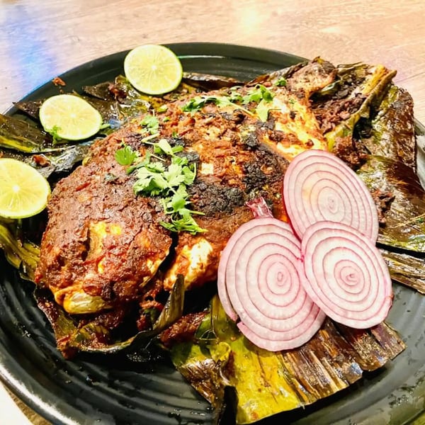Indian-style whole grilled fish, garnished with cilantro, lime wedges, and red onion slices.
