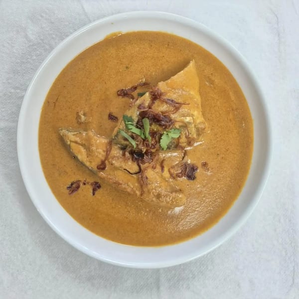 Indian fish curry in a white bowl, garnished with fried onions and fresh cilantro.