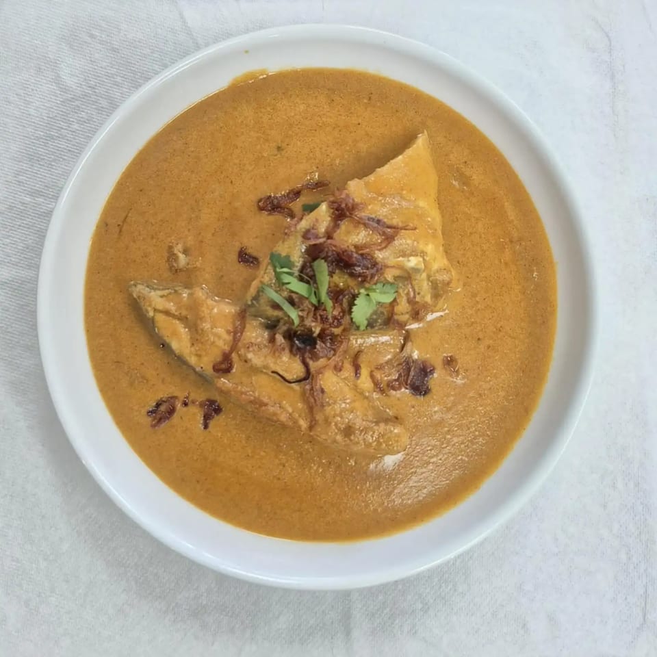 Indian fish curry in a white bowl, garnished with fried onions and fresh cilantro.