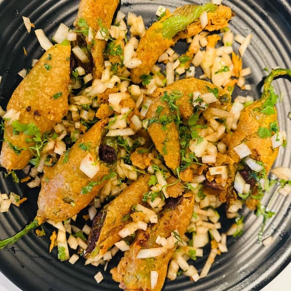 Fried green chili peppers, garnished with chopped onions and cilantro, on a black plate.