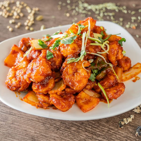 Cumin N Eat's Indian chili paneer, a vibrant red dish with paneer, onions, and green garnishes.