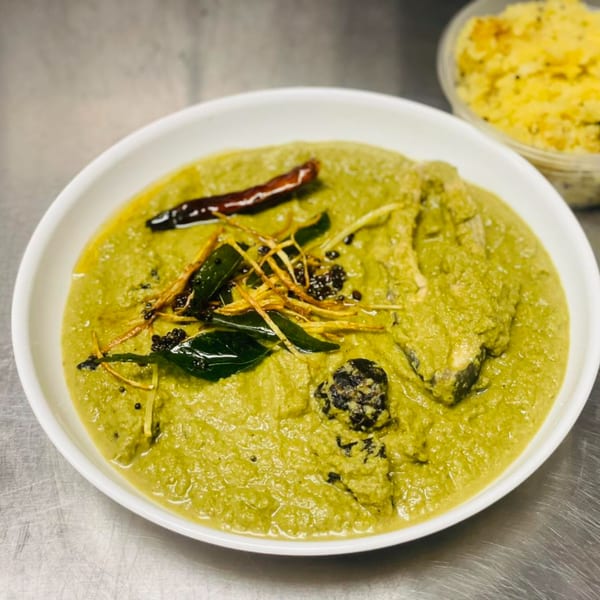 Indian green curry with fish, garnished with dried chilies, curry leaves, and ginger.
