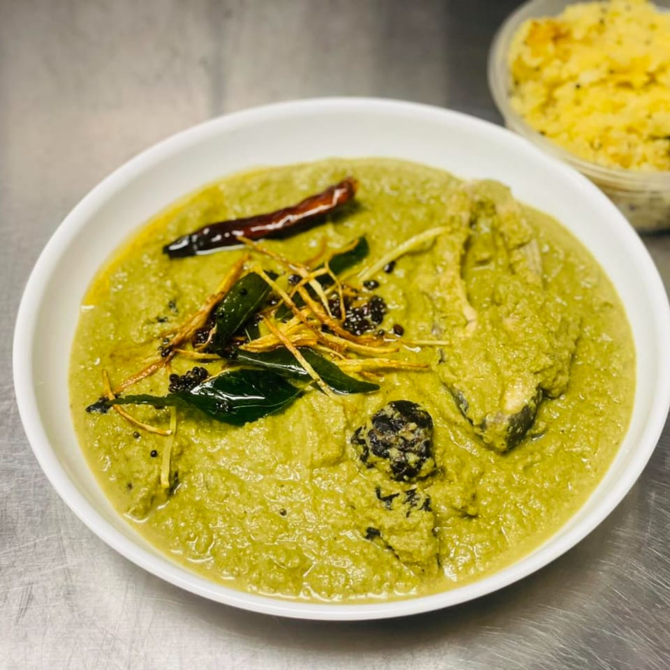 Indian green curry with fish, garnished with dried chilies, curry leaves, and ginger.