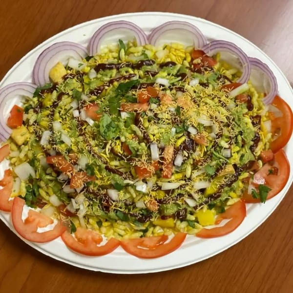 A vibrant Indian Bhel Puri dish, topped with chopped onions, tomatoes, cilantro, and sauces.