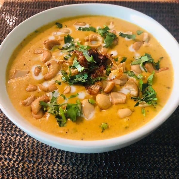 Creamy Indian curry with cashews, peanuts, fried onions, and fresh cilantro in a white bowl.