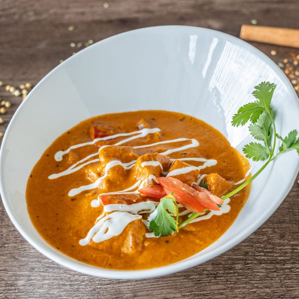 Cumin N Eat's Indian butter chicken, garnished with cream, tomatoes, and cilantro in a white bowl.