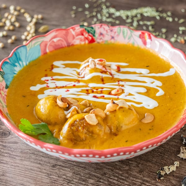 Indian curry with chicken, cashews, and cream drizzle in a floral bowl on a wooden table.