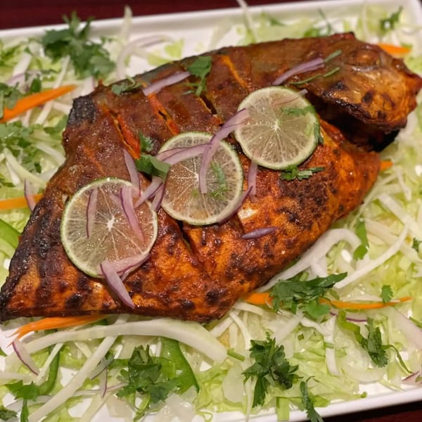 Whole grilled Indian fish, garnished with lime slices, red onions, and fresh cilantro on a bed of lettuce.