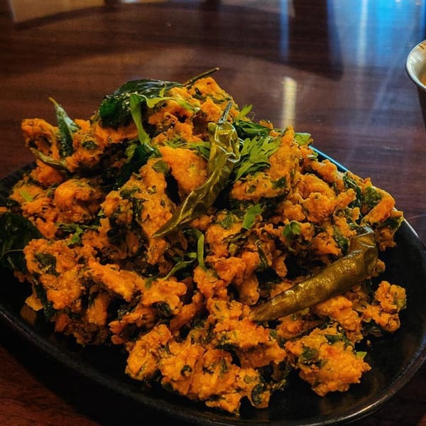 A close-up of Cumin N Eat's Indian pakora, golden-fried and garnished with green chilies and herbs.
