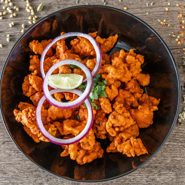 Cumin N Eat's Indian chicken pakora, garnished with red onion rings, lime, and cilantro.