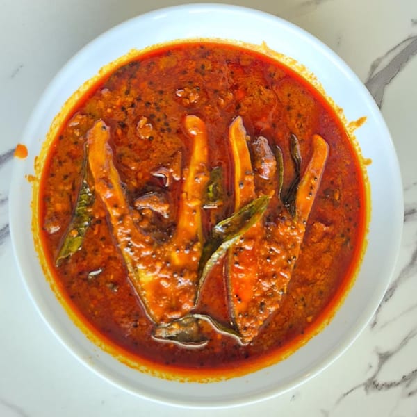 A vibrant Indian fish curry, with pieces of fish in a rich, red, spiced gravy, served in a white bowl.