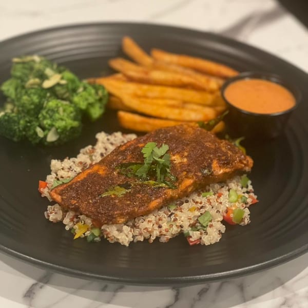 Indian spiced salmon on quinoa with broccoli, sweet potato fries, and dipping sauce.